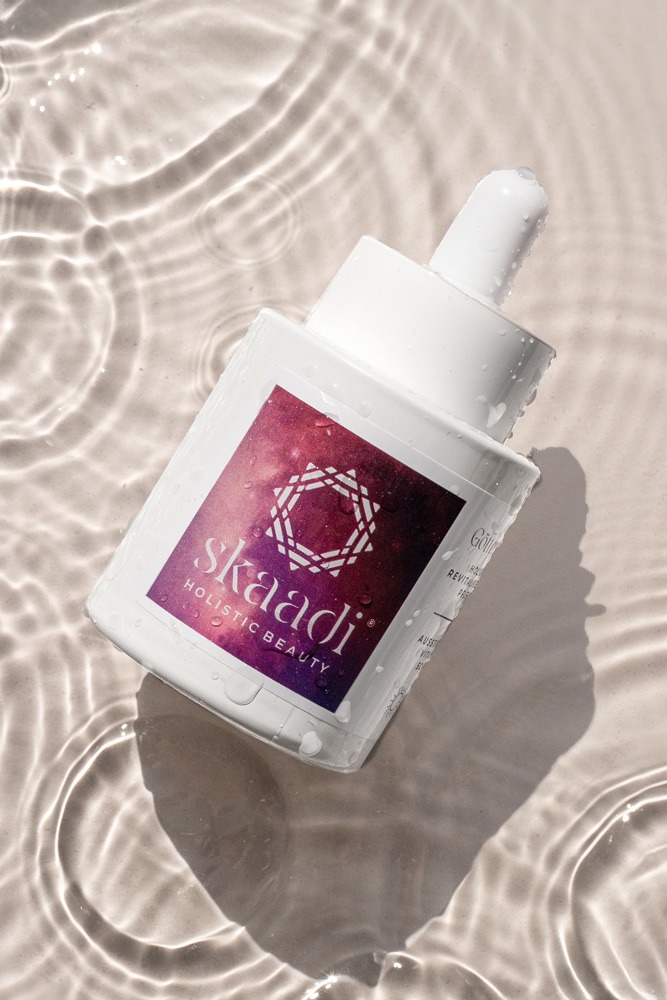 Göttertränen Elixier Pflegeöl Flasche auf beigem nassen Untergrund