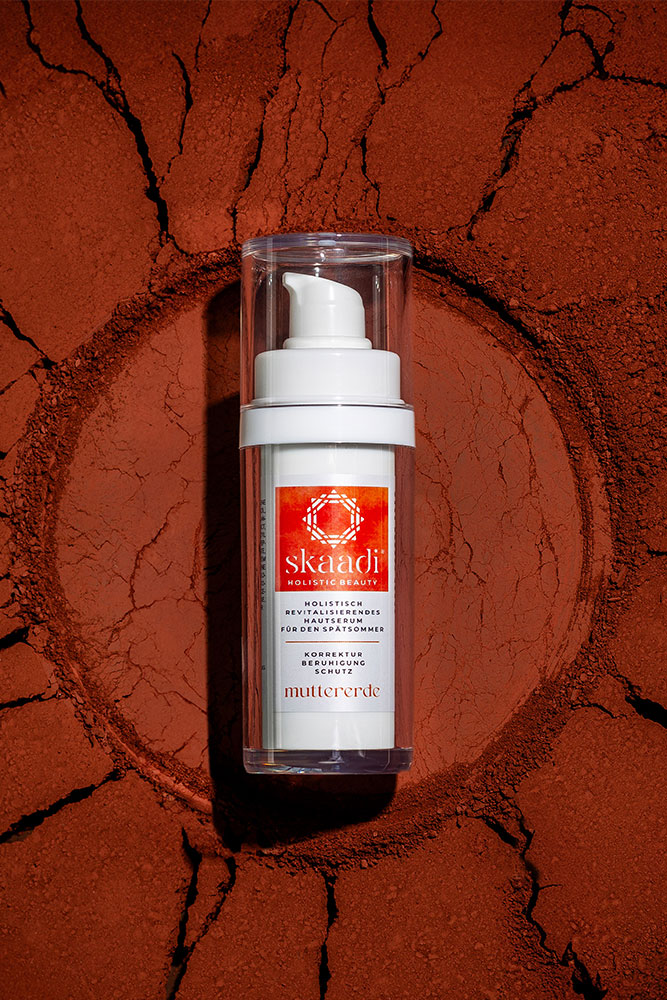 skaadi® Muttererde Elementra Spätsommerserum liegt auf rotbraunem pudrigen Untergrund mit Rissen