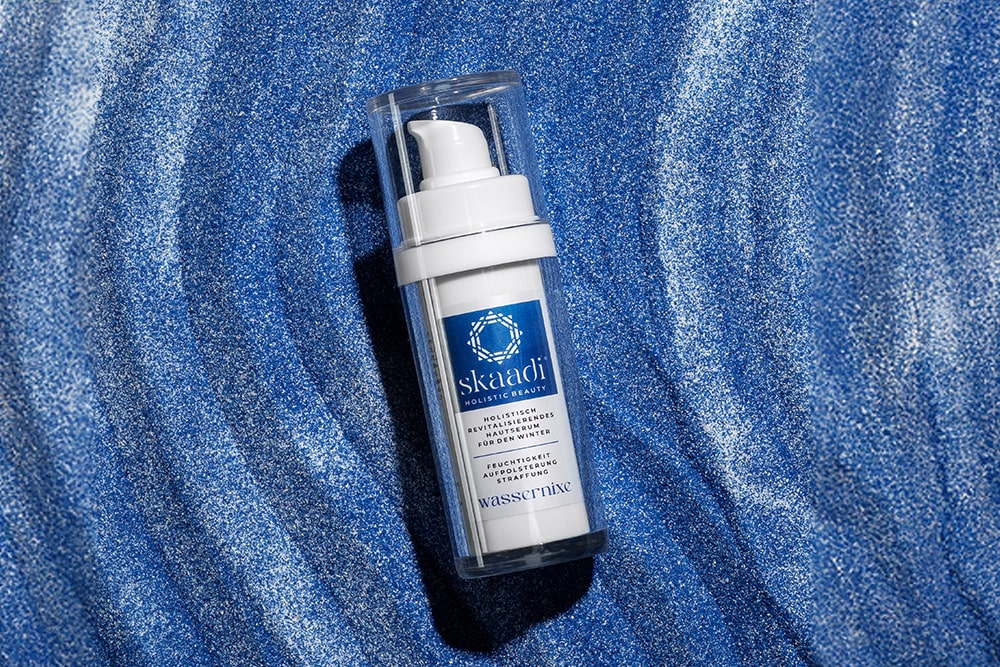 skaadi® Wassernixe Elementra Winterserum liegt auf blau-weißem sandigen Untergrund