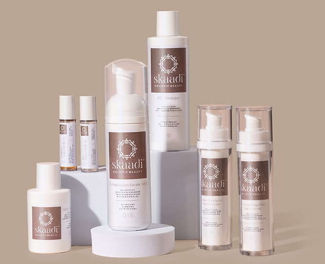 alle skaadi Basispflegeprodukte nebeneinander aufgereiht auf verschiedenen Höhen auf beigem Hintergrund